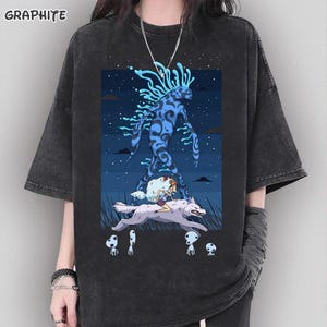 May include: Graphite gray t-shirt featuring a fantasy illustration. The graphic depicts a blue spirit-like figure, a girl riding a wolf, and forest spirits against a starry night sky. The shirt has short sleeves and a relaxed fit.
