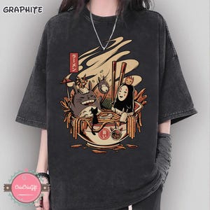 May include: Graphite gray t-shirt featuring a colorful illustration of anime characters in a ramen bowl. The design includes a smiling Totoro, a black cat, and other figures. The word "Ramen" is written in Japanese.