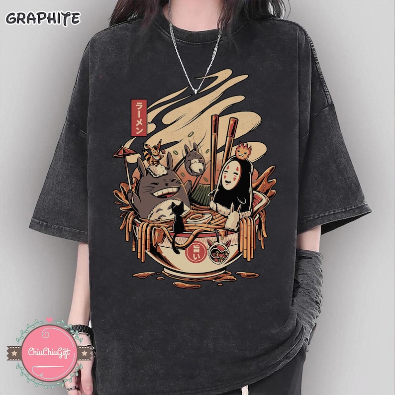 May include: Graphite gray t-shirt featuring a colorful illustration of anime characters in a ramen bowl. The design includes a smiling Totoro, a black cat, and other figures. The word "Ramen" is written in Japanese.
