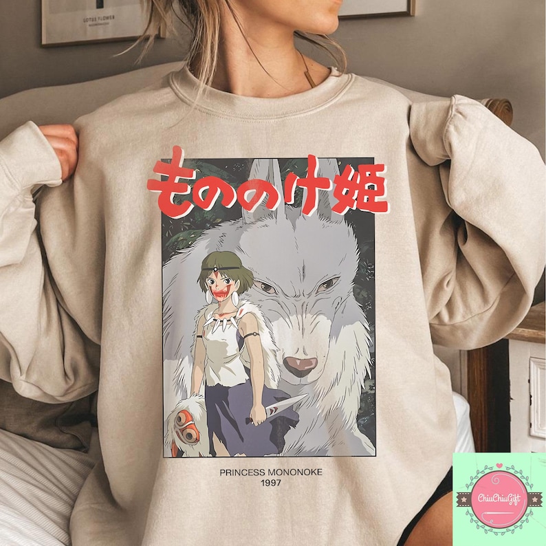 May include: Beige sweatshirt with a graphic from the animated film Princess Mononoke. The design features a female character and a wolf, with Japanese text above and the text "PRINCESS MONONOKE 1997" below the image.