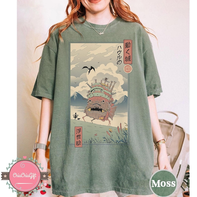 Pu&ograve; includere: T-shirt verde muschio con un'illustrazione in stile anime giapponese. L'opera raffigura un castello in movimento con testo giapponese. La maglietta ha una vestibilit&agrave; ampia e maniche corte. La parola "Moss" &egrave; stampata in basso a destra.