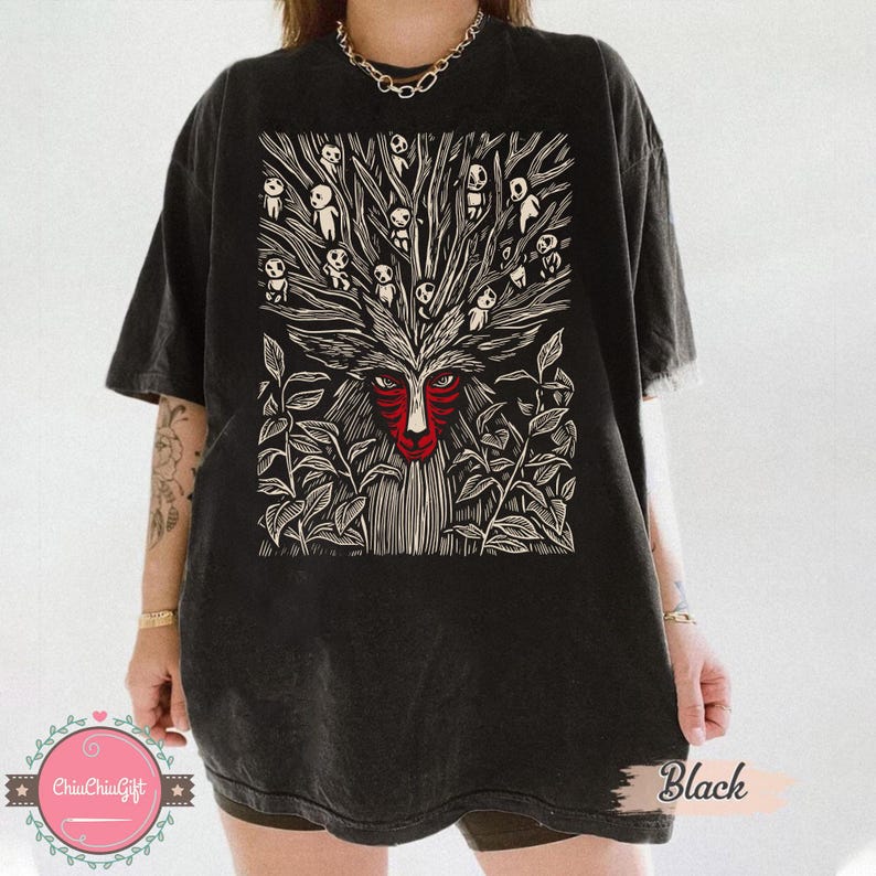 以下が含まれることがあります： 黒いTシャツ。赤い顔と白と黒のディテールを持つ森の精霊の詳細なグラフィックが特徴です。デザインには、小さなフィギュアのある木のような構造が含まれています。「Black」の文字がTシャツにプリントされています。