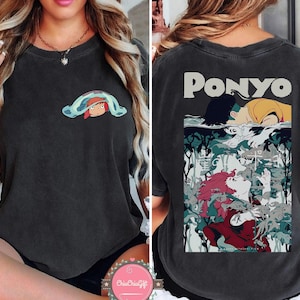 May include: Dark gray t-shirt featuring a front graphic of a cartoon character under a blue and green blanket. The back of the shirt displays the word "PONYO" above a colorful illustration of characters in an underwater scene.