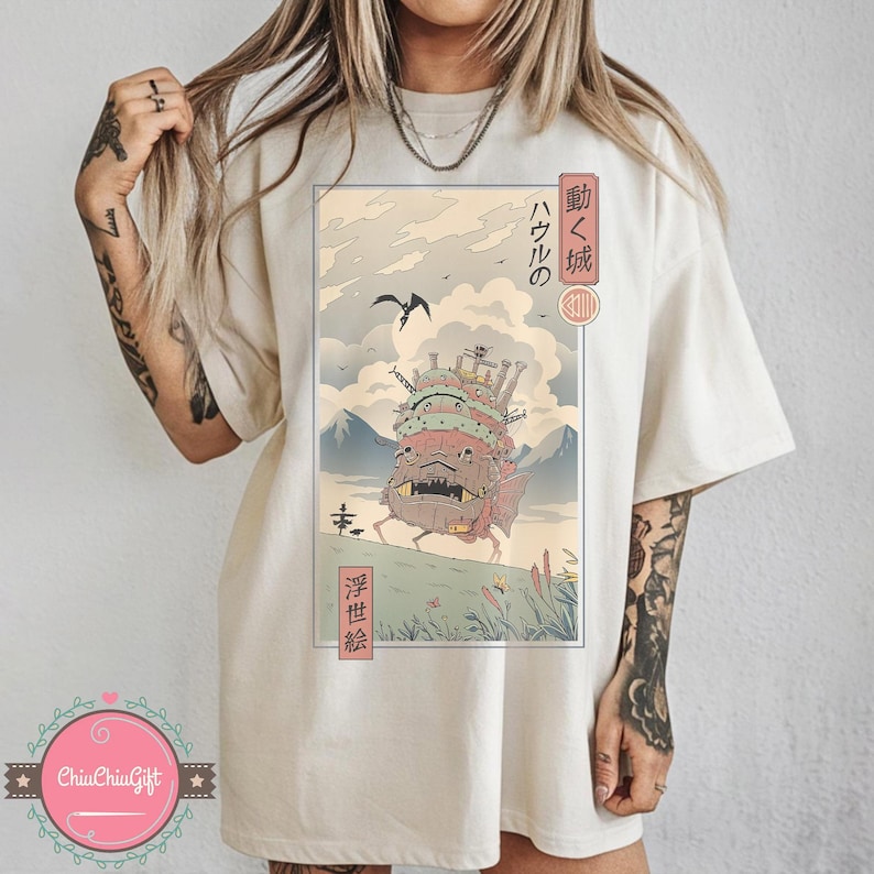 Pu&ograve; includere: T-shirt color crema con un'illustrazione incorniciata del castello in movimento del film d'animazione "Il castello errante di Howl". L'opera d'arte include testo giapponese e un paesaggio con montagne, un uccello e il castello. La maglietta &egrave; di vestibilit&agrave; ampia.