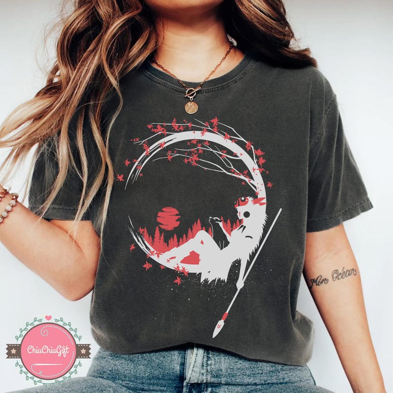 May include: Dark gray t-shirt featuring a white and red graphic of a figure reclining under a tree with a spear. The design includes a red sun and forest scene within a circular frame. The shirt has a crew neck.