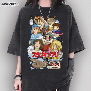 May include: Dark gray t-shirt featuring a colorful graphic of Studio Ghibli characters. The design includes Japanese text and the words "THE LOFT CINEMA". The shirt has short sleeves and a relaxed fit.