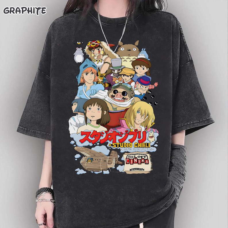 May include: Dark gray t-shirt featuring a colorful graphic of Studio Ghibli characters. The design includes Japanese text and the words "THE LOFT CINEMA". The shirt has short sleeves and a relaxed fit.