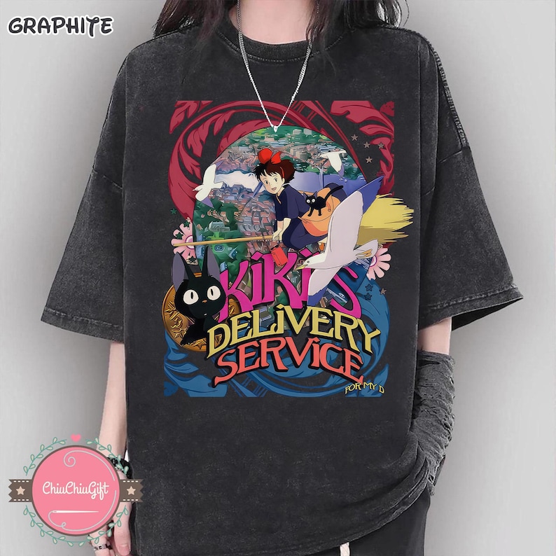 May include: Graphite-coloured t-shirt with a vibrant graphic from "Kiki's Delivery Service." The design showcases Kiki on a broom, a black cat, and the text "Kiki's Delivery Service." The shirt has short sleeves and a relaxed fit.