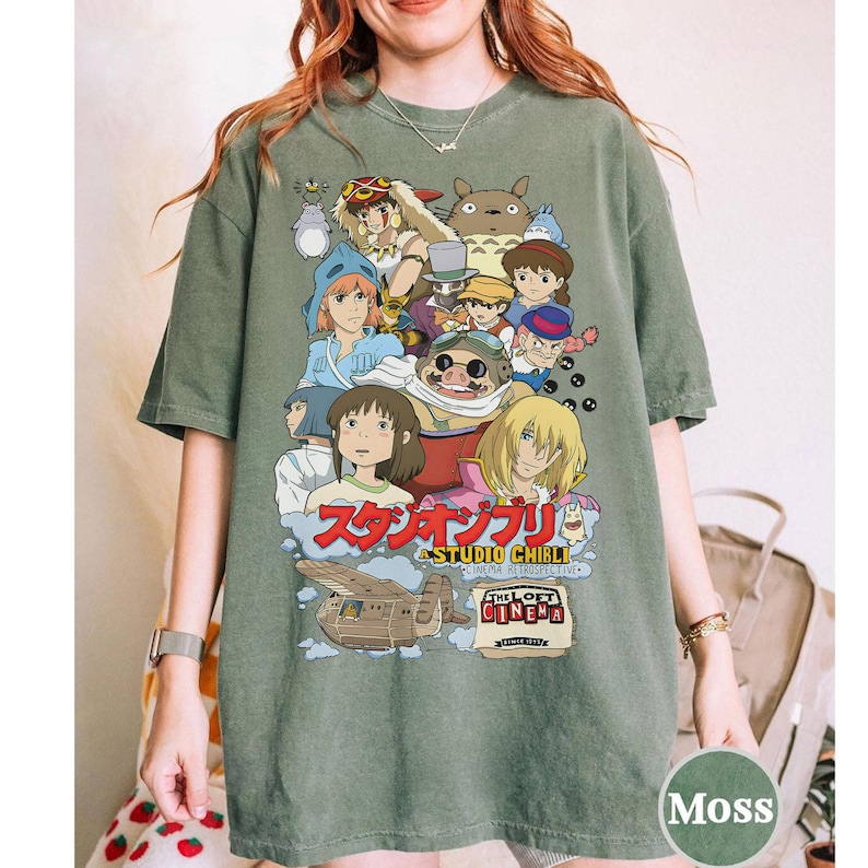 May include: Moss green t-shirt featuring a colorful graphic of Studio Ghibli characters. The design includes Japanese text and the words "The Loft Cinema" and "Cinema Retrospective". The shirt is a relaxed fit.