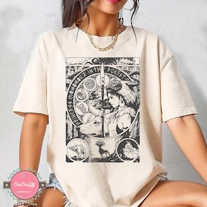 Puede incluir: Camiseta color crema con un gr&aacute;fico en blanco y negro de una mujer sosteniendo una lanza, con un lobo y un ciervo. El texto "PRINCESS MONONOKE IN THE FOREST" est&aacute; impreso alrededor de la imagen central. La camiseta tiene mangas cortas.