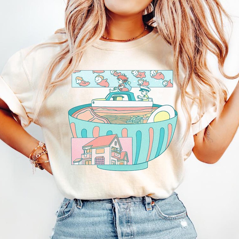 Puede incluir: Camiseta color crema con una ilustraci&oacute;n caprichosa. El dise&ntilde;o representa un gran cuenco de ramen con un barco y dos figuras. Arriba, nadan peces de dibujos animados. Abajo, se muestra una casa. La camiseta es de material suave.