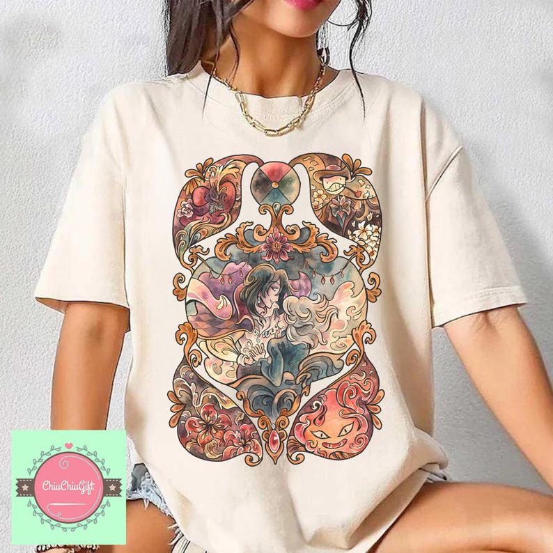 May include: Cream-colored t-shirt featuring a colorful, ornate graphic design. The design includes floral elements, figures, and a central image of two people embracing. The overall style is reminiscent of stained glass art.