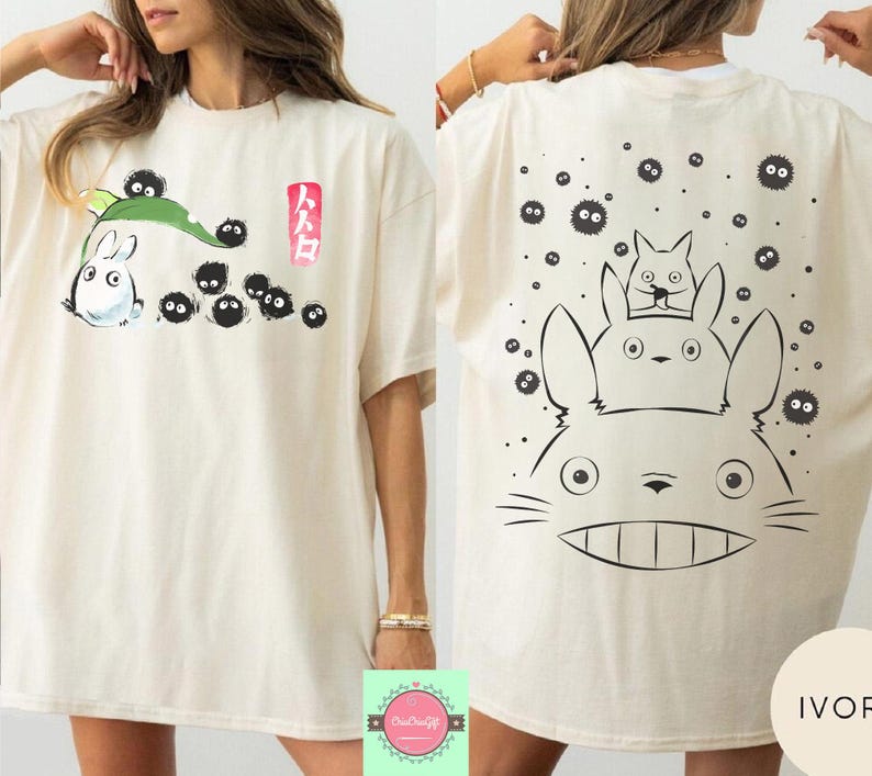 May include: Ivory-colored t-shirt featuring a front graphic of a white cartoon character with a green leaf and black soot sprites, and Japanese text. The back of the shirt has a large graphic of the same character with two smaller characters and more soot sprites.