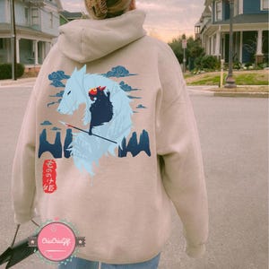 May include: Beige hoodie with a graphic of a wolf and a figure with a spear, with Japanese text. The design includes blue clouds and mountain-like shapes. The hoodie has a drawstring hood and a kangaroo pocket.