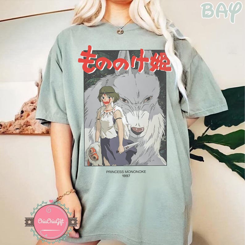May include: A pale green t-shirt with a graphic from the animated film Princess Mononoke. The graphic features the Japanese title in red, a character illustration, and the text "PRINCESS MONONOKE 1997". The shirt has short sleeves and a loose fit.