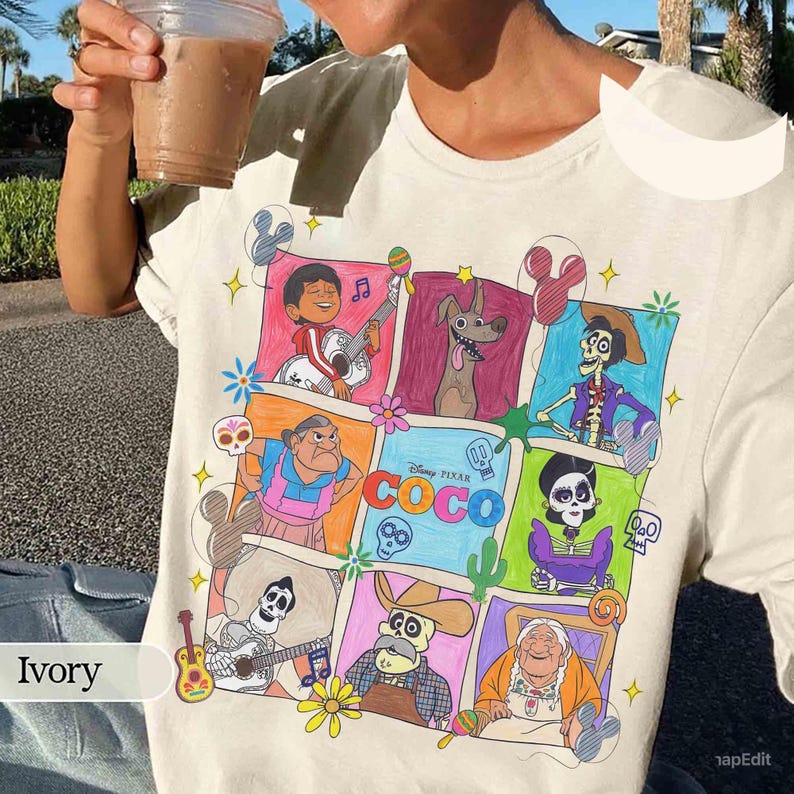 May include: Ivory-colored t-shirt featuring a colorful graphic of characters from the Disney Pixar movie "Coco." The design includes various characters in a grid-like arrangement, with the movie's title prominently displayed. The shirt is made of a soft material.