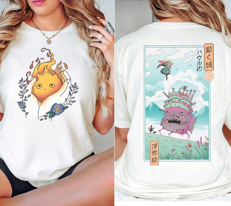 K&ouml;nnte beinhalten: Cremefarbenes T-Shirt mit Cartoon-Illustration. Auf der Vorderseite ist eine feurige Kreatur in H&auml;nden zu sehen, umgeben von floralen Akzenten. Die R&uuml;ckseite zeigt eine gerahmte Szene mit einem sich bewegenden Schloss und japanischem Text.