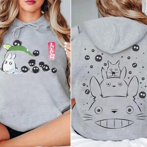 May include: Gray hoodie featuring a front graphic of a white rabbit-like creature with black soot sprites and a green leaf. The back of the hoodie displays a large graphic of the same creature with two smaller ones. The Japanese text is visible.