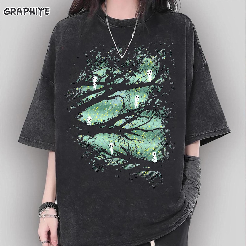 May include: Graphite-colored t-shirt with a nature-themed graphic. The design features a tree with white, ghost-like figures against a teal and yellow background. The shirt has short sleeves and a relaxed fit.