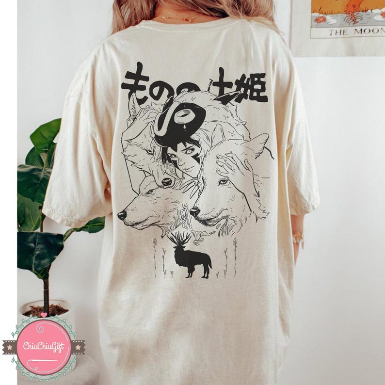 May include: Cream-colored t-shirt featuring a black and white illustration of a character surrounded by wolves and a deer. Japanese text is above the illustration. The shirt has short sleeves and a relaxed fit.