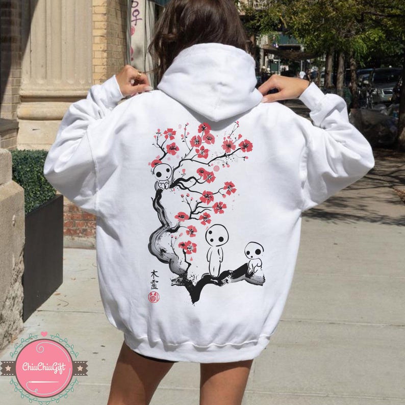 May include: White hoodie featuring a Japanese-inspired design on the back. The graphic includes a stylized tree with pink blossoms and three small, whimsical figures. The Japanese characters are also visible.