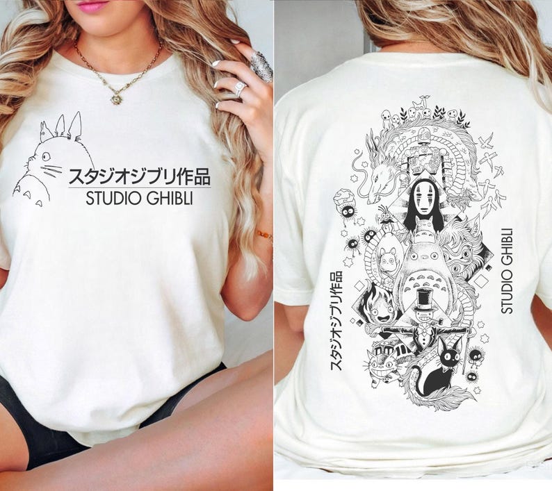May include: Cream-colored t-shirt featuring a black and white illustration of Studio Ghibli characters. The front displays a Totoro design with Japanese text and "STUDIO GHIBLI." The back showcases a detailed graphic of various characters and the text "STUDIO GHIBLI."
