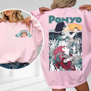 May include: Pink sweatshirt featuring a colorful graphic from the animated film "Ponyo." The front has a small cartoon image, while the back displays a larger illustration with the film's title in teal letters. The design includes characters and aquatic elements.