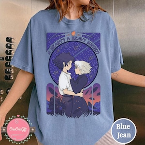 Puede incluir: Camiseta azul vaquera con un dise&ntilde;o de la pel&iacute;cula de animaci&oacute;n, El castillo ambulante. El dise&ntilde;o muestra a dos personajes abraz&aacute;ndose, sobre un cielo estrellado, con el texto "A HEART'S A HEAVY BURDEN".