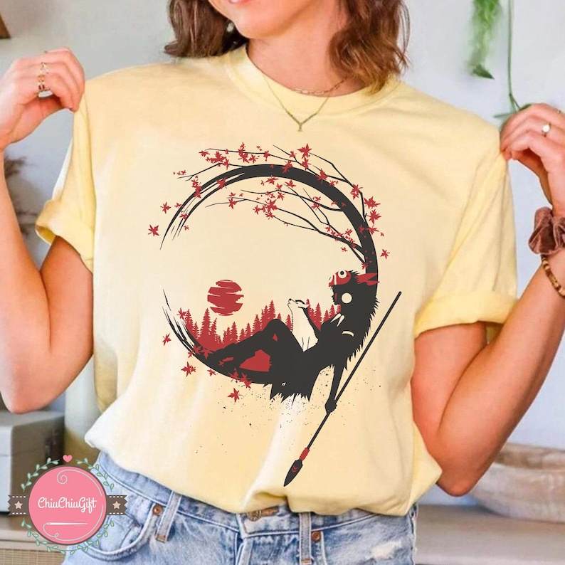 May include: A light yellow t-shirt featuring a black and red graphic design. The design depicts a silhouette of a figure reclining in a forest scene, with a red sun and tree branches. A spear is also included in the design.