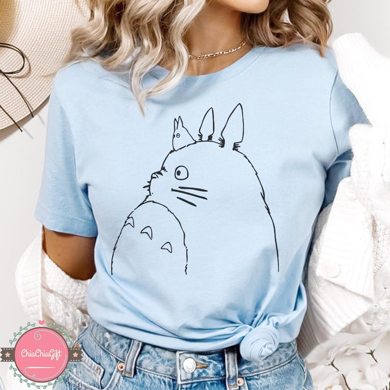 Puede incluir: Camiseta azul claro con un dibujo lineal negro de un personaje de Totoro y un peque&ntilde;o conejo. El dise&ntilde;o est&aacute; centrado en la camiseta. La camiseta est&aacute; hecha de un material suave.