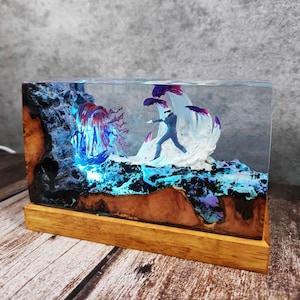 May include: A rectangular resin art piece featuring a miniature figure in a suit, set against a backdrop of blue and purple illuminated elements. The base is made of wood, and the artwork is encased in clear resin.