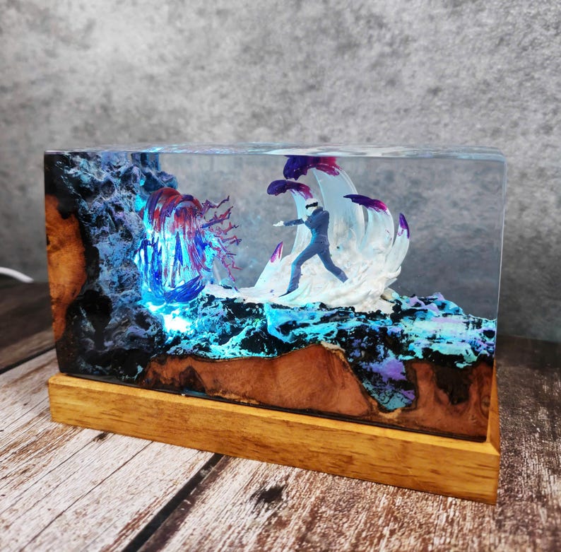 May include: A rectangular resin art piece featuring a miniature figure in a suit, set against a backdrop of blue and purple illuminated elements. The base is made of wood, and the artwork is encased in clear resin.