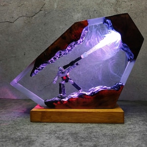 May include: A unique resin lamp featuring a robot figure with a weapon, emitting a bright light. The lamp is encased in a clear resin with a wooden base and accents. The design incorporates red and purple hues, creating a striking visual effect.