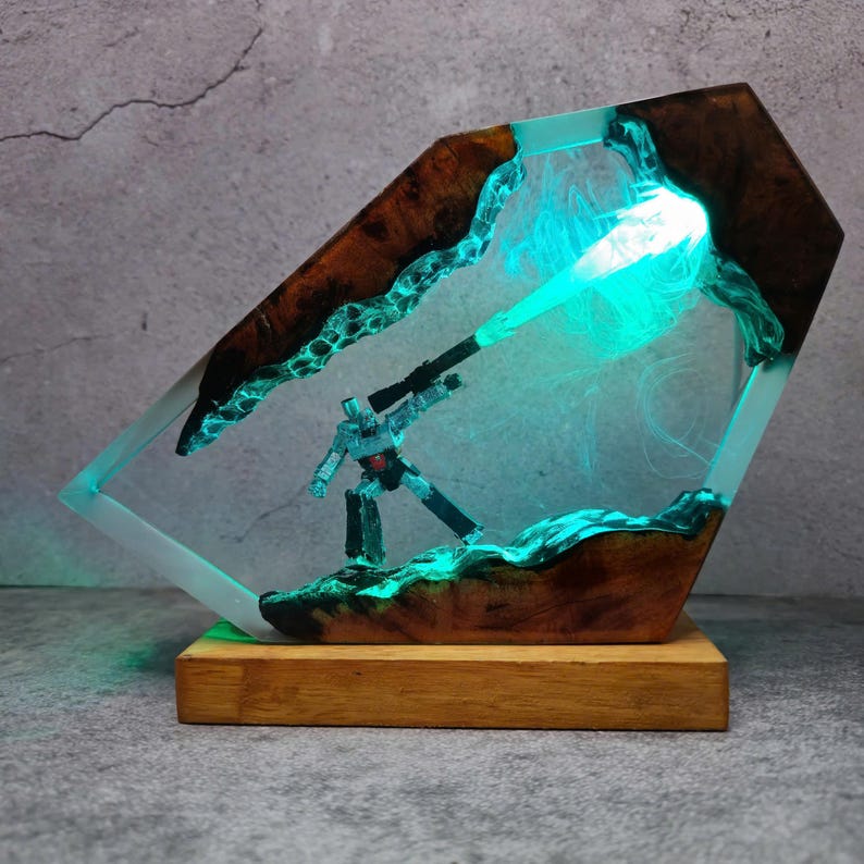 May include: A unique resin art piece featuring a robot figure with a glowing green beam. The artwork is encased in a clear resin with wooden accents and a wooden base. The piece has a futuristic, sci-fi theme.