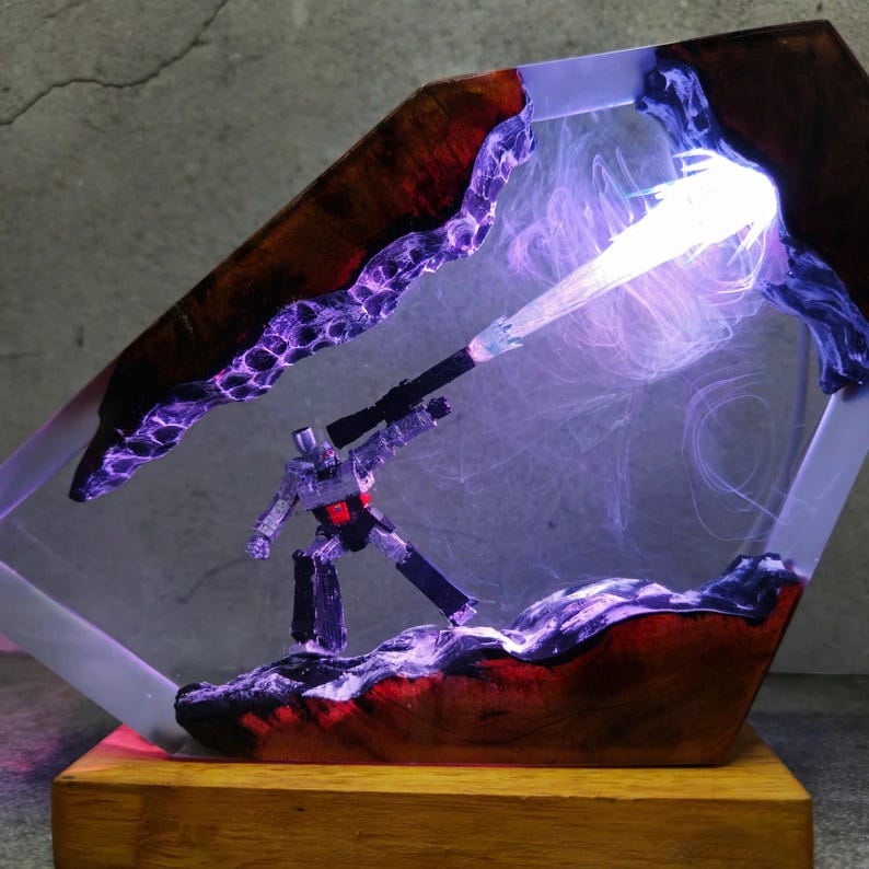 May include: A unique resin art piece featuring a silver robot figure with a black weapon, set within a clear, geometric frame. The frame has a wood-grain border with purple and red accents, and a bright light beam. The base is made of wood.
