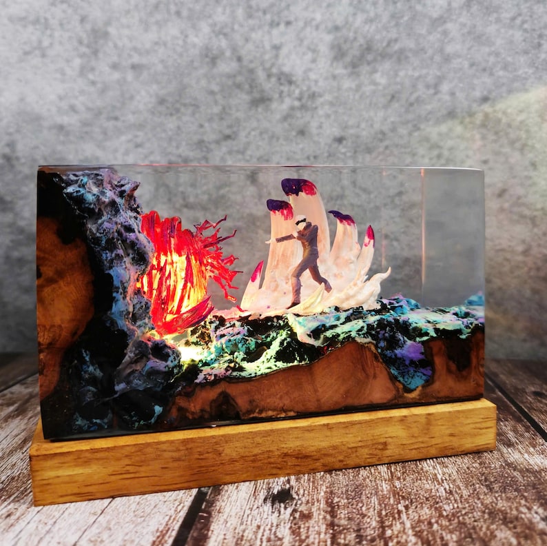 May include: A rectangular resin art piece featuring a miniature figure running towards a red, glowing structure. The base is wood, and the resin contains colorful, textured elements. The piece is illuminated from within, creating a dramatic effect.