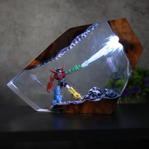 May include: A colorful Voltron action figure inside a clear resin block with a wooden frame. The figure is holding a sword and a glowing energy beam. The resin block is on a dark surface.