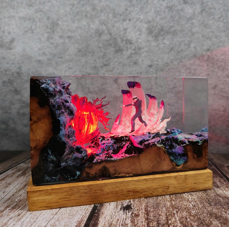 May include: A rectangular resin art piece with a wooden base. The artwork features a miniature figure running towards a glowing red and pink landscape. The resin is clear, showcasing the detailed scene with vibrant colors and textures.