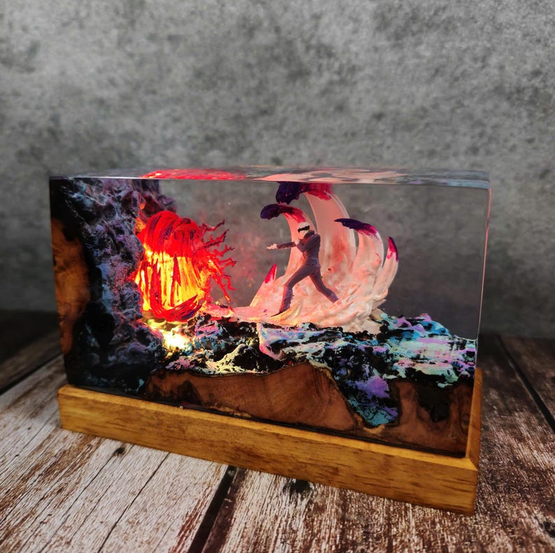 May include: A rectangular resin art piece featuring a miniature figure facing a fiery, red-lit structure. The base is wood, and the scene is encased in clear resin. The artwork has a fantasy theme with vibrant colors.