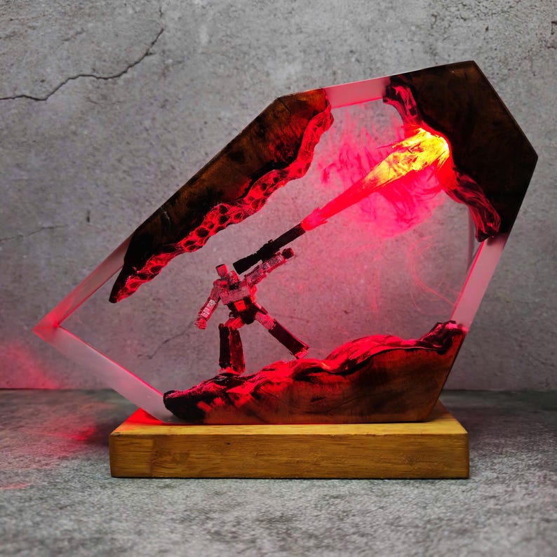 May include: A unique resin art piece featuring a small robot figure with a red laser beam. The artwork is encased in a clear, geometric frame with a wooden base. The interior is illuminated with red light.