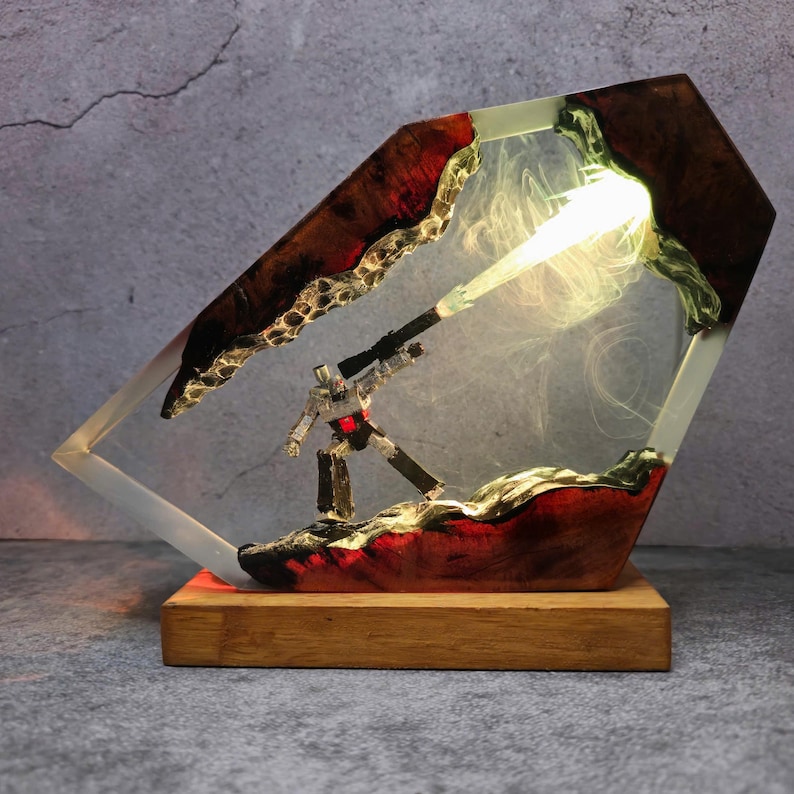 May include: A unique lamp featuring a robot figure encased in a clear resin structure. The resin is accented with red and brown tones, and the lamp sits on a wooden base. The robot is holding a weapon, and the lamp emits a bright light.