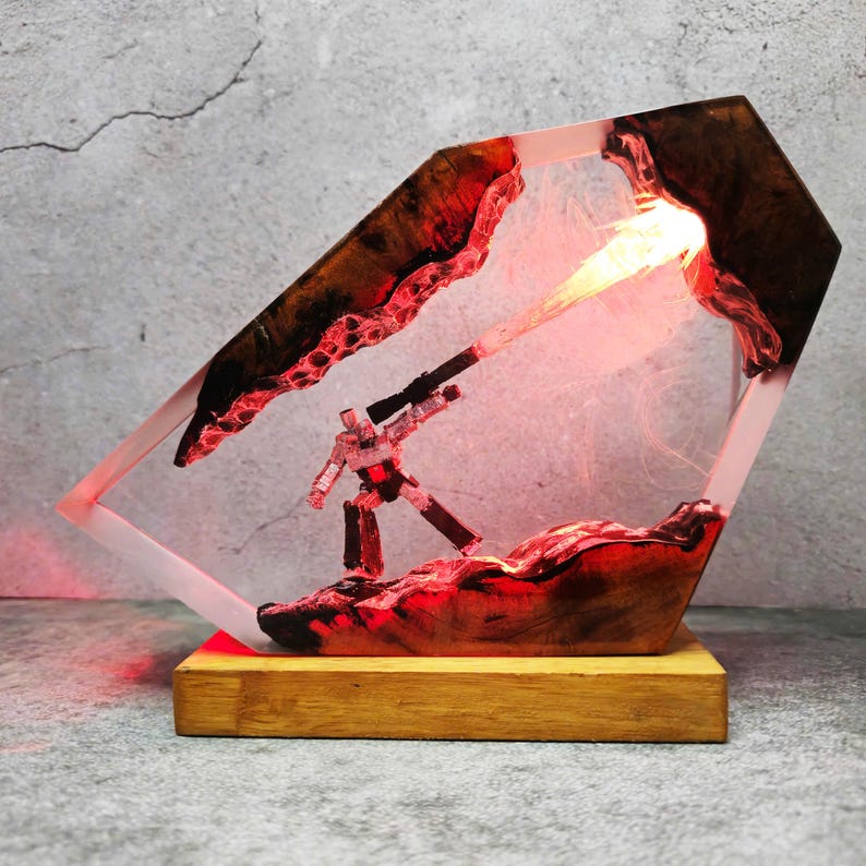 May include: A unique resin lamp featuring a small figure with a weapon, set within a clear, geometric frame. The lamp has a wooden base and a red and brown color scheme, with a bright light emanating from the center.
