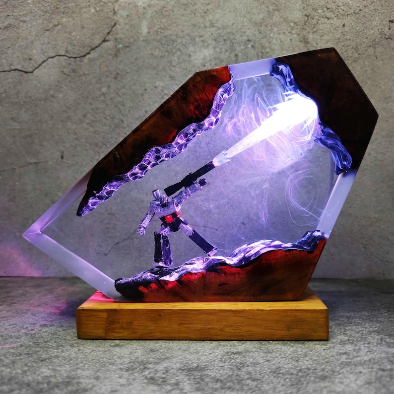 May include: A unique resin lamp featuring a robot figure, set within a clear, geometric structure. The lamp has a wooden base and is illuminated with purple and white light, creating a striking visual effect. The resin is accented with dark red and brown wood.