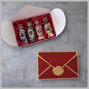 May include: A white box containing four small glass bottles with cork stoppers, filled with colourful beads. Each bottle has a letter on it. The box is filled with red paper shreds. A red envelope with gold trim and a gold seal is below.
