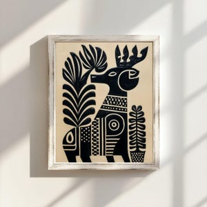 May include: Black and white framed art print featuring a stylized deer with intricate patterns and plant elements. The artwork has a folk art style, with a cream-colored background and a distressed white frame. The deer has a crown and is surrounded by stylized plants.