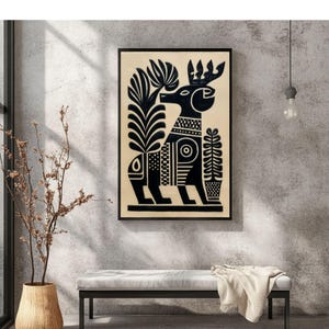 May include: Black and cream-colored framed art print featuring a stylized deer design. The deer is depicted in black with intricate patterns and floral elements. The artwork is displayed on a neutral-colored wall, with a bench and decorative vase in the foreground.