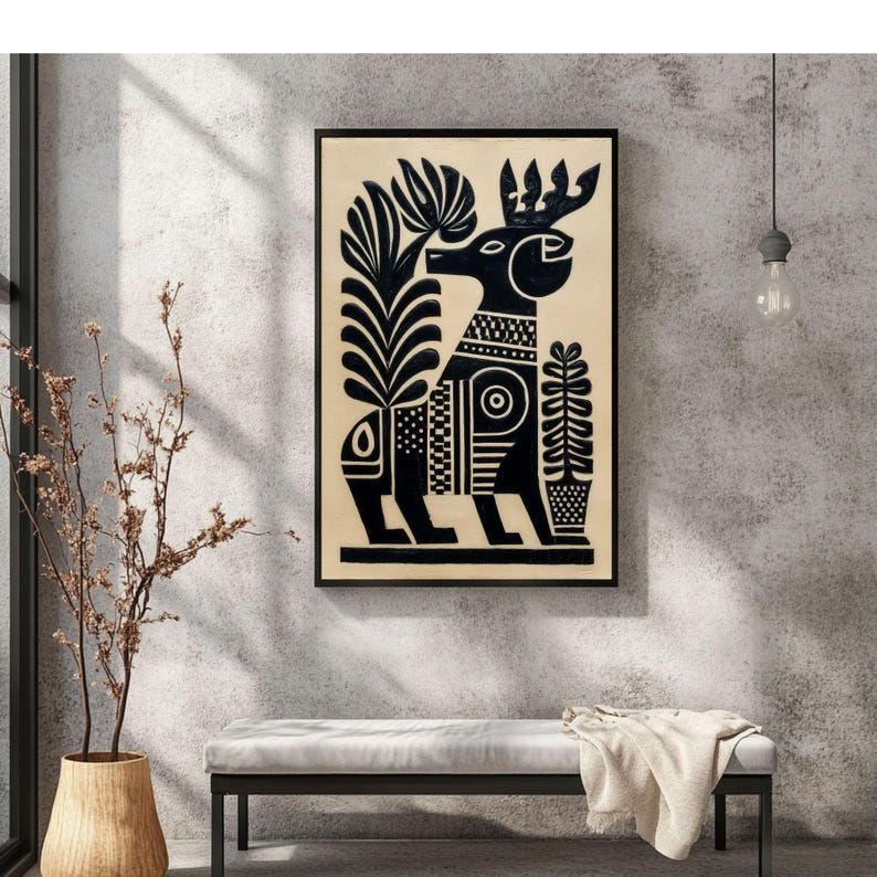 May include: Black and cream-colored framed art print featuring a stylized deer design. The deer is depicted in black with intricate patterns and floral elements. The artwork is displayed on a neutral-colored wall, with a bench and decorative vase in the foreground.