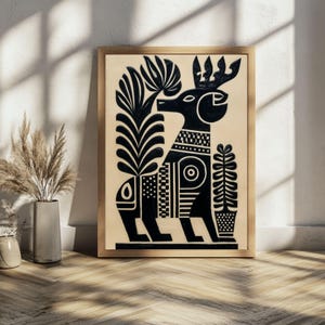 May include: Black and white folk art print of a stylized deer with a crown and decorative patterns. The artwork is framed in a light wood frame and set against a neutral background. The print features a symmetrical design with floral and geometric elements.