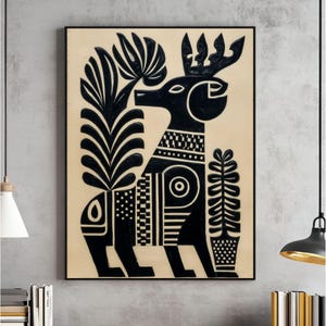 May include: Black and white folk art style painting of a deer-like creature with large antlers and decorative patterns. The artwork is framed in a black rectangular frame and set against a beige background.