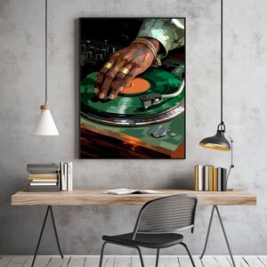 Pode incluir: Uma obra de arte emoldurada retrata uma m&atilde;o com an&eacute;is e pulseiras douradas em uma vitrola verde. A obra de arte tem uma moldura preta e &eacute; exibida em uma mesa de madeira. A imagem tem um estilo art&iacute;stico moderno.